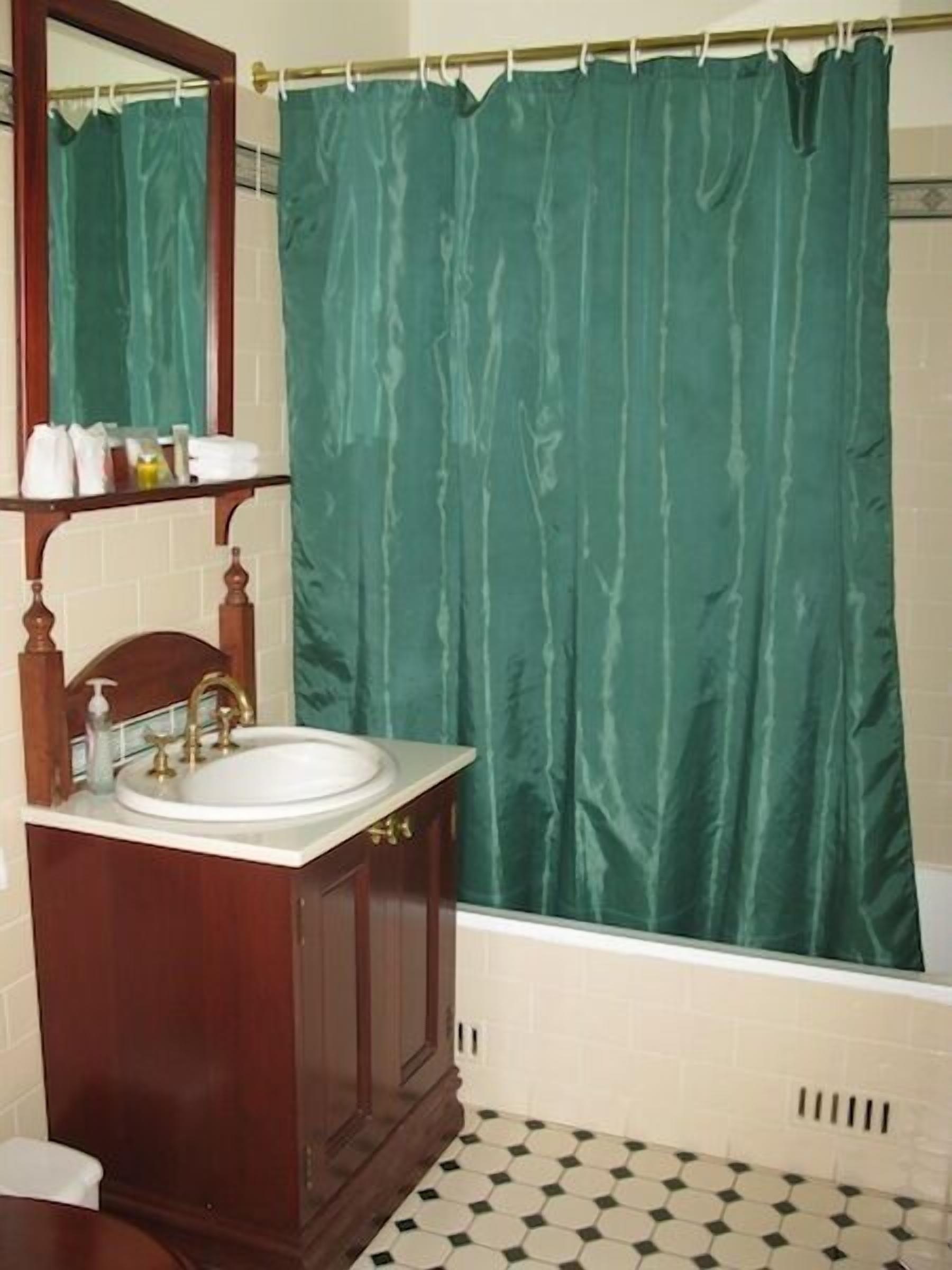 A bathroom with a wooden vanity, a white sink, and a green shower curtain.