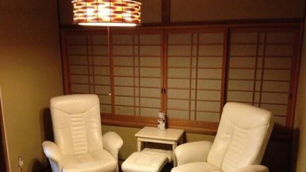 A room with two white leather armchairs, a small table, and a traditional Japanese shoji screen in the background. - Fuji Hostel (Onomichi)