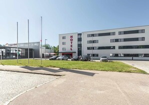 Un moderno edificio de hotel con un llamativo letrero 'HOTEL', un estacionamiento con varios coches y una cafetería en primer plano.