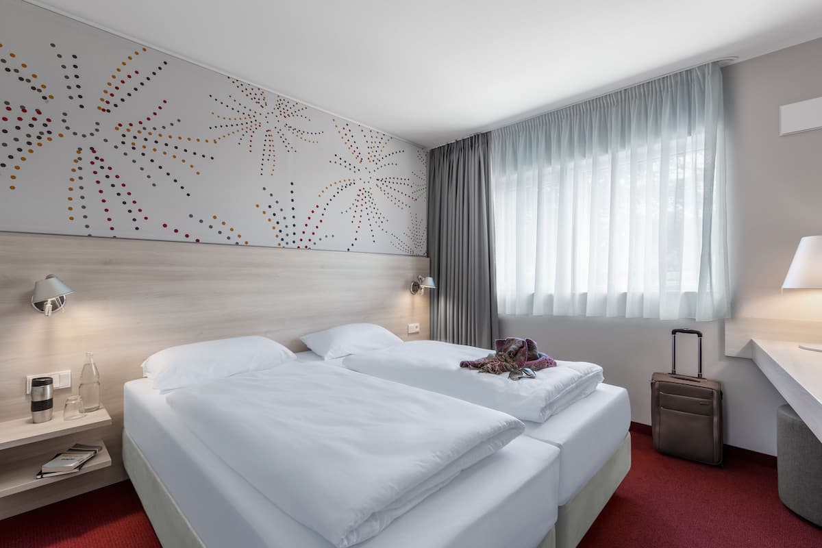 A hotel room with two beds, a desk, a suitcase, and a wall with a dot pattern.