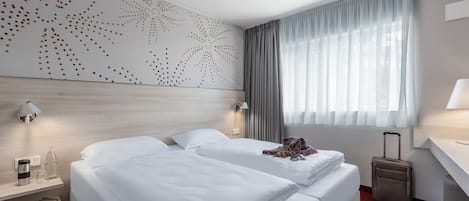 Ein Hotelzimmer mit zwei Betten, einem Schreibtisch, einem Koffer und einer Wand mit einem Punktmuster.