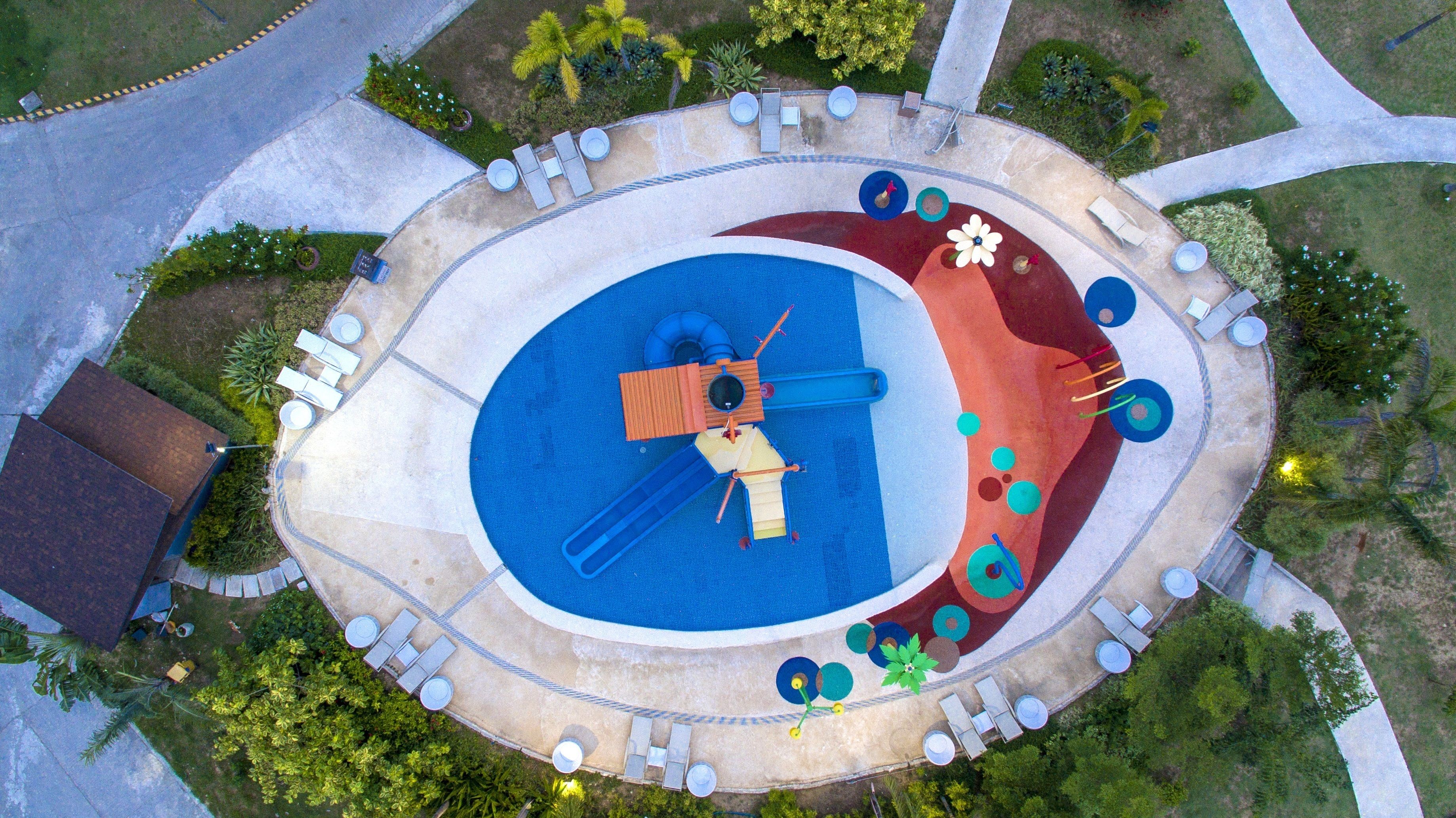 An aerial view of a circular pool area with a slide, lounge chairs, and a small deck.