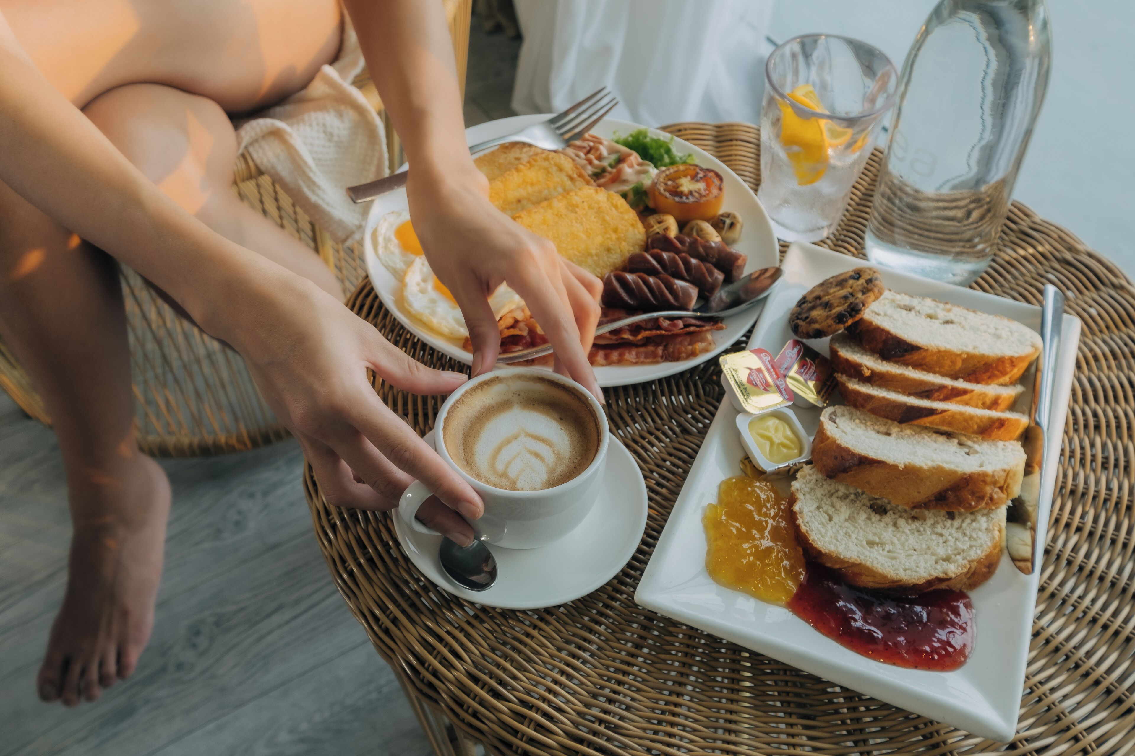 Una escena de desayuno con un plato de comida, una taza de café y un vaso de agua sobre una mesa de fibras naturales.