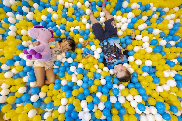 Two children lying in a ball pit filled with yellow and white balls. - Solea Seaview Resort (Cordova)