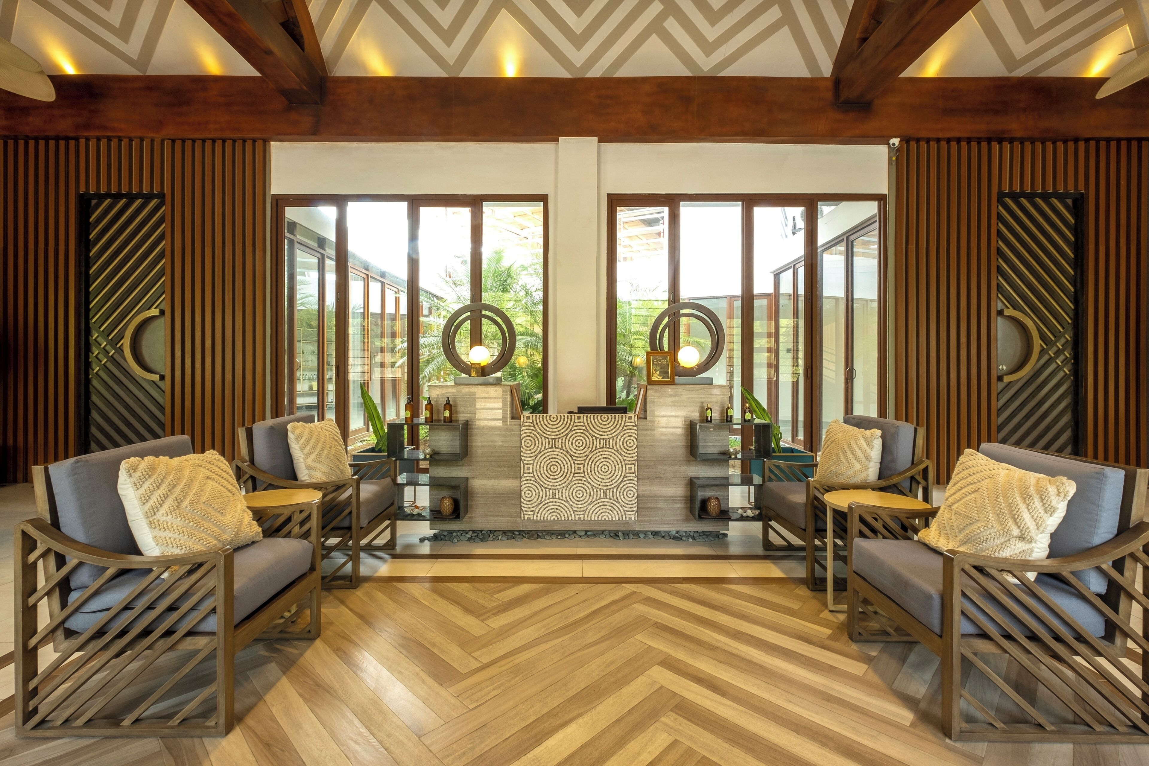 A modern lobby with wooden flooring, two sofas with cushions, a patterned rug, and a reception desk.