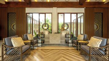 A modern lobby with wooden flooring, two sofas with cushions, a patterned rug, and a reception desk.