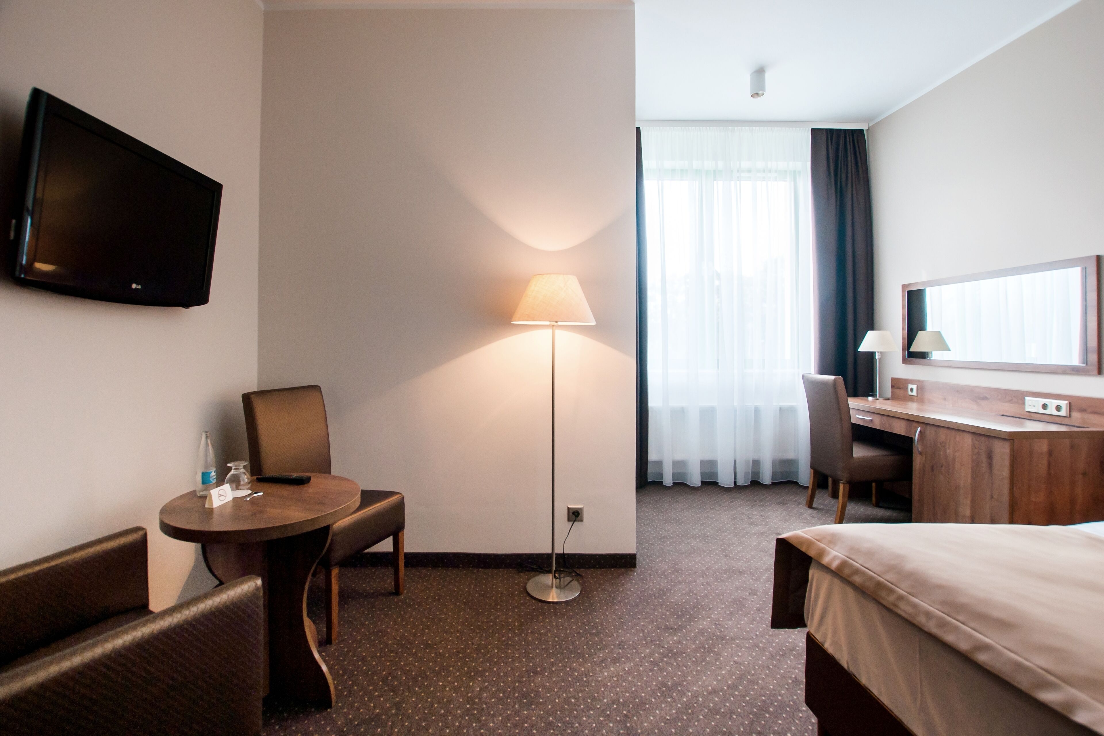 Una camera d'albergo con un letto, una scrivania, una sedia, un tavolo, una televisione e una lampada.
