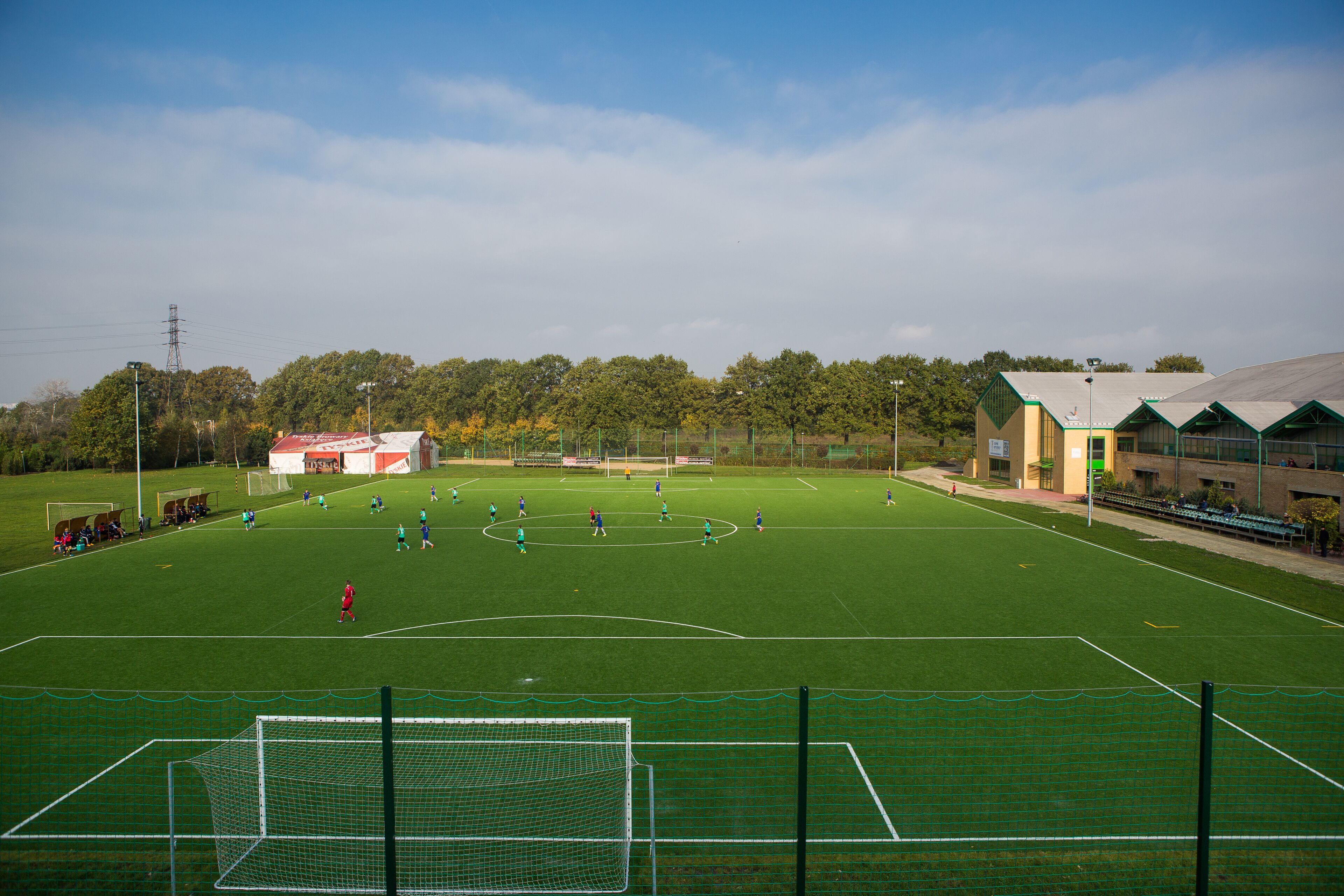 Ein Fußballfeld mit Toren, einem Zaun und einem Gebäude mit Gründach im Hintergrund.