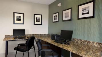 Un espacio de trabajo con dos escritorios, cada uno con una computadora y una silla. Hay cuadros en la pared.