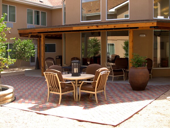 An outdoor patio with a round table and four chairs, a large planter, and a pergola structure. - Baymont by Wyndham Hobbs (Hobbs)