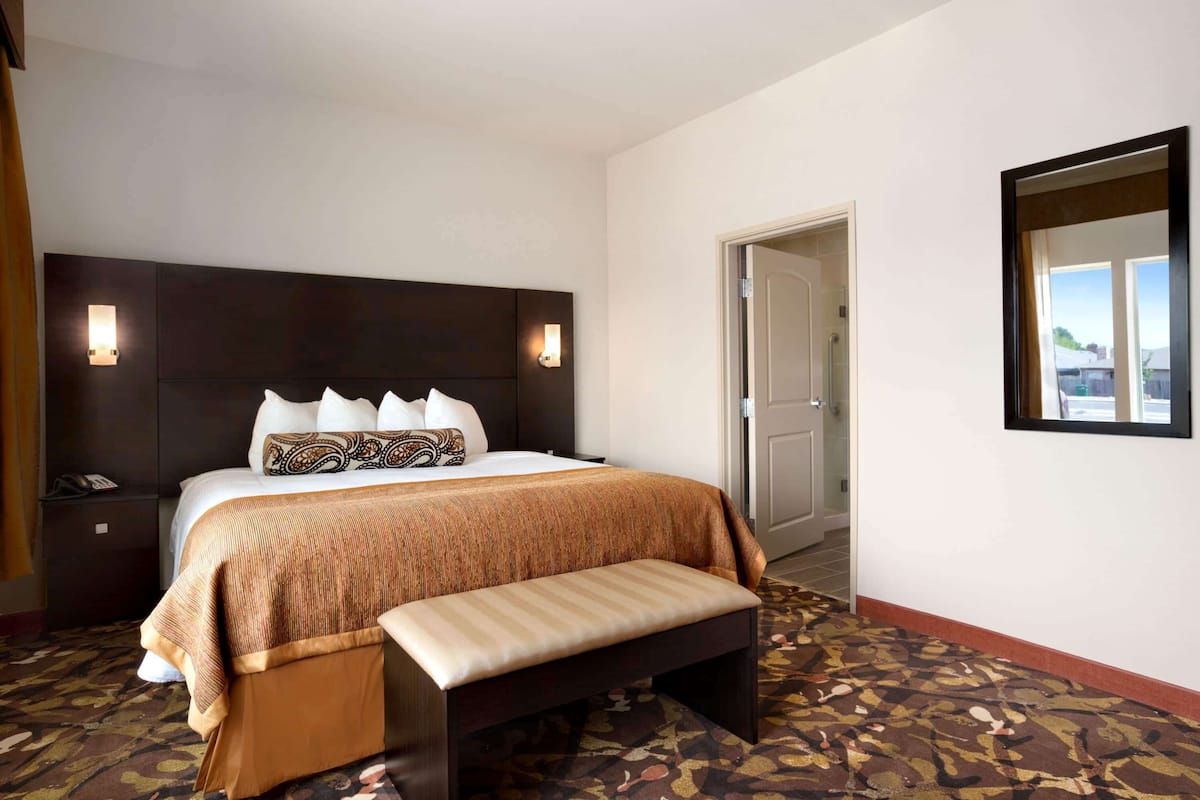Une chambre d’hôtel avec un grand lit, une banquette, une table de chevet et un miroir fixé au mur.