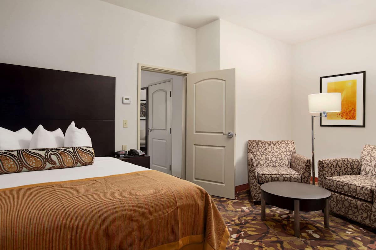 Une chambre d’hôtel avec un lit, une chaise, une petite table et une porte donnant sur une autre pièce.