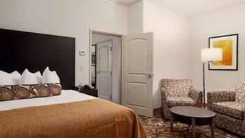 A hotel room with a bed, a chair, a small table, and a door leading to another room.