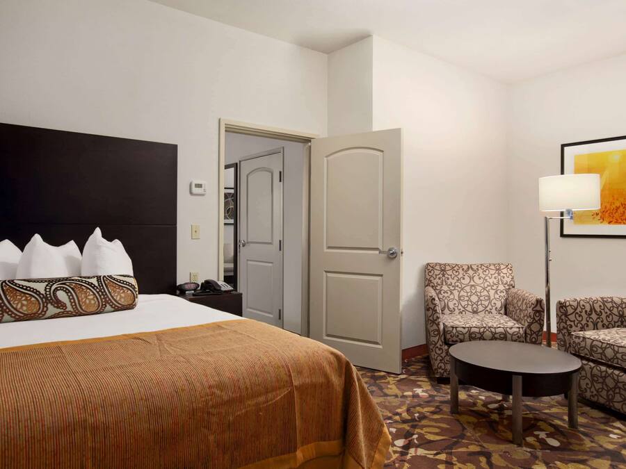 A hotel room with a bed, a chair, a small table, and a door leading to another room.