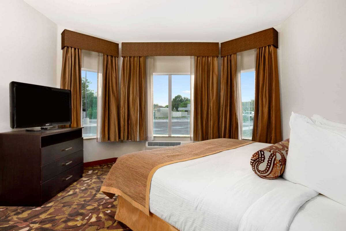 Une chambre d’hôtel avec un grand lit, un téléviseur à écran plat posé sur une commode, et une vue sur l’extérieur grâce à une grande fenêtre avec des rideaux.