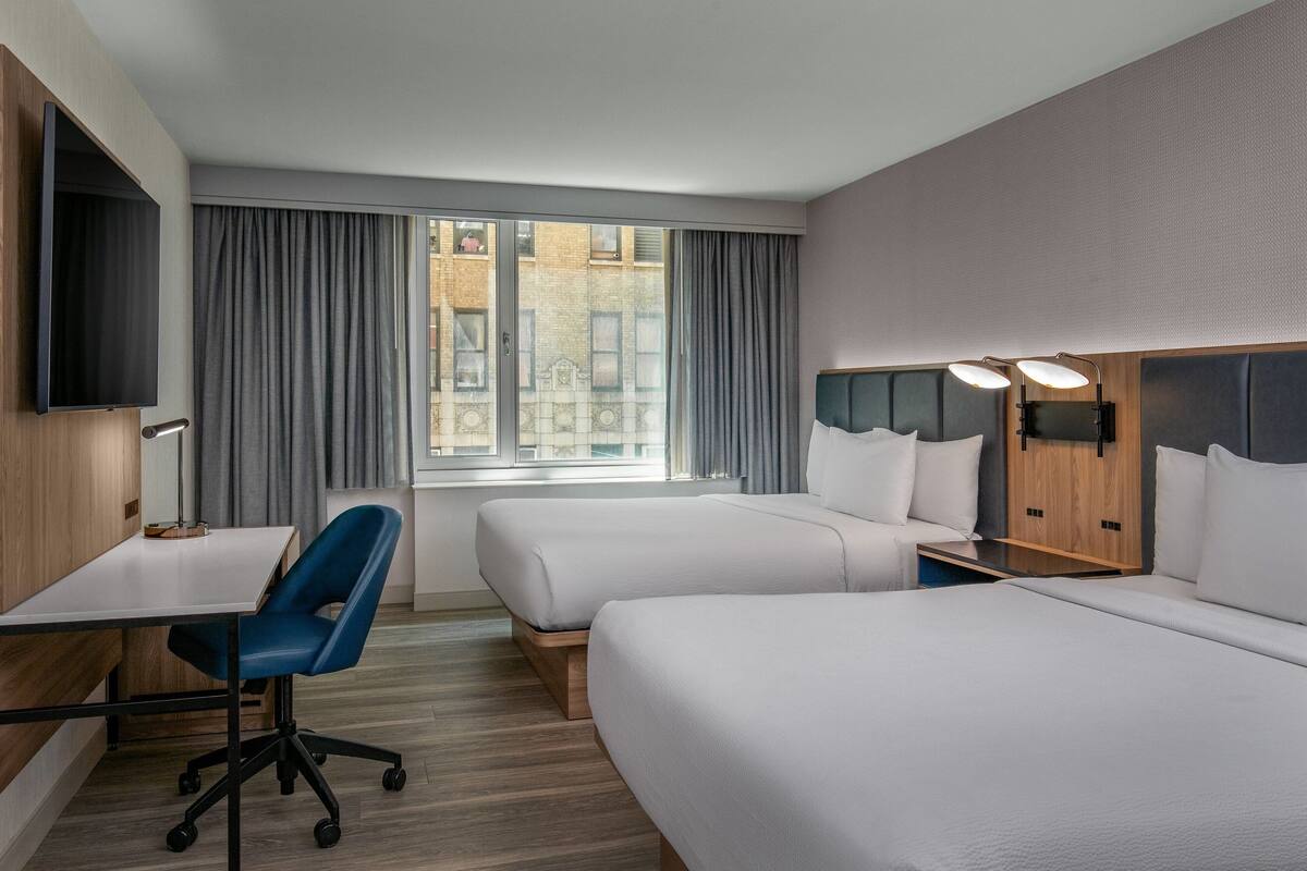 Hotelkamer met twee bedden, een bureau, een stoel, een televisie en een raam met gordijnen.