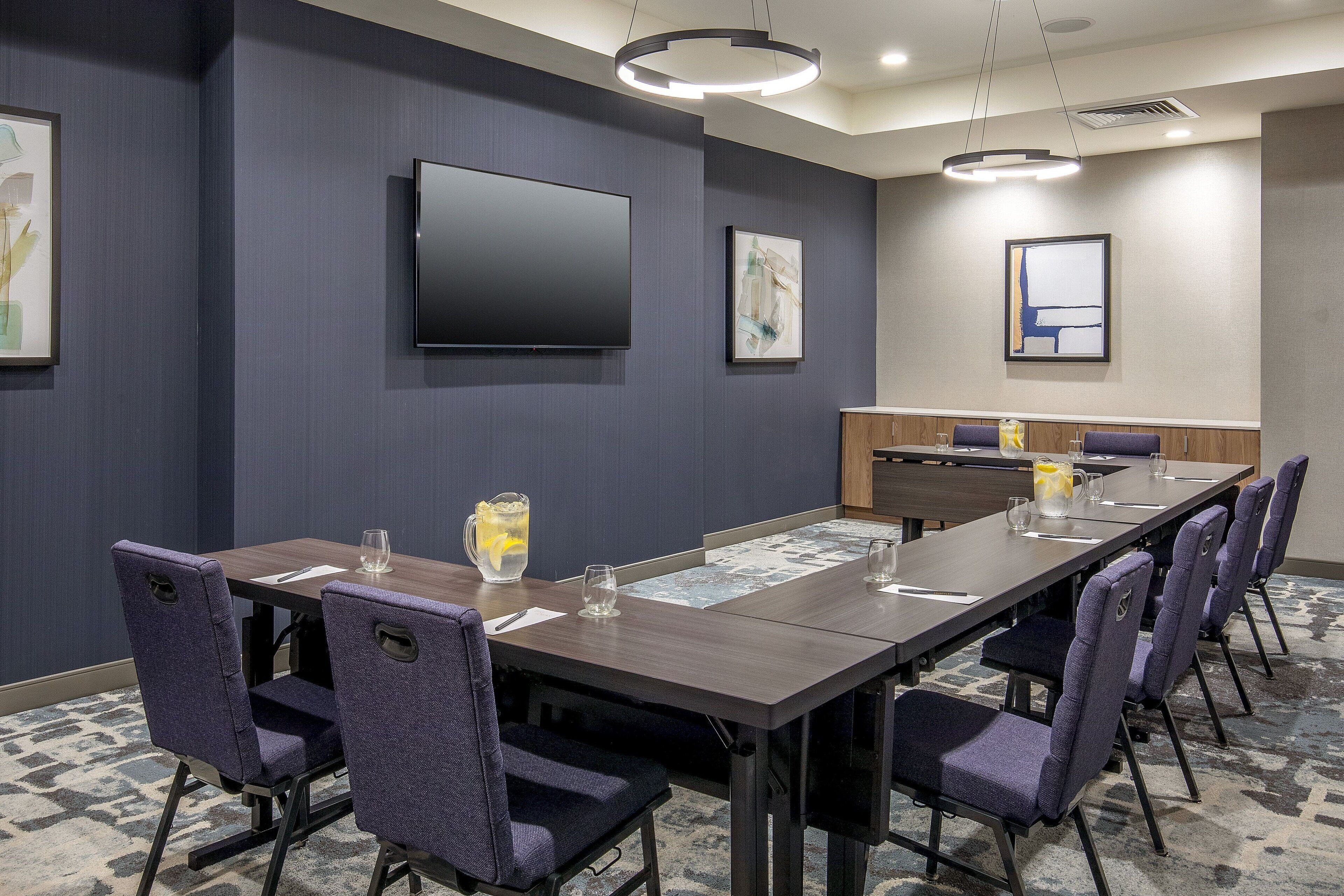 A conference room with a long table, chairs, a flat-screen TV, and artwork on the walls.