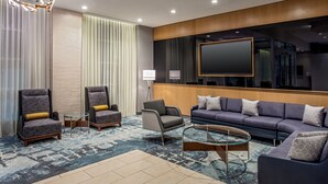 Een moderne hotel lobby met een grote bank, twee fauteuils, een salontafel en een grote flatscreen televisie aan de muur.