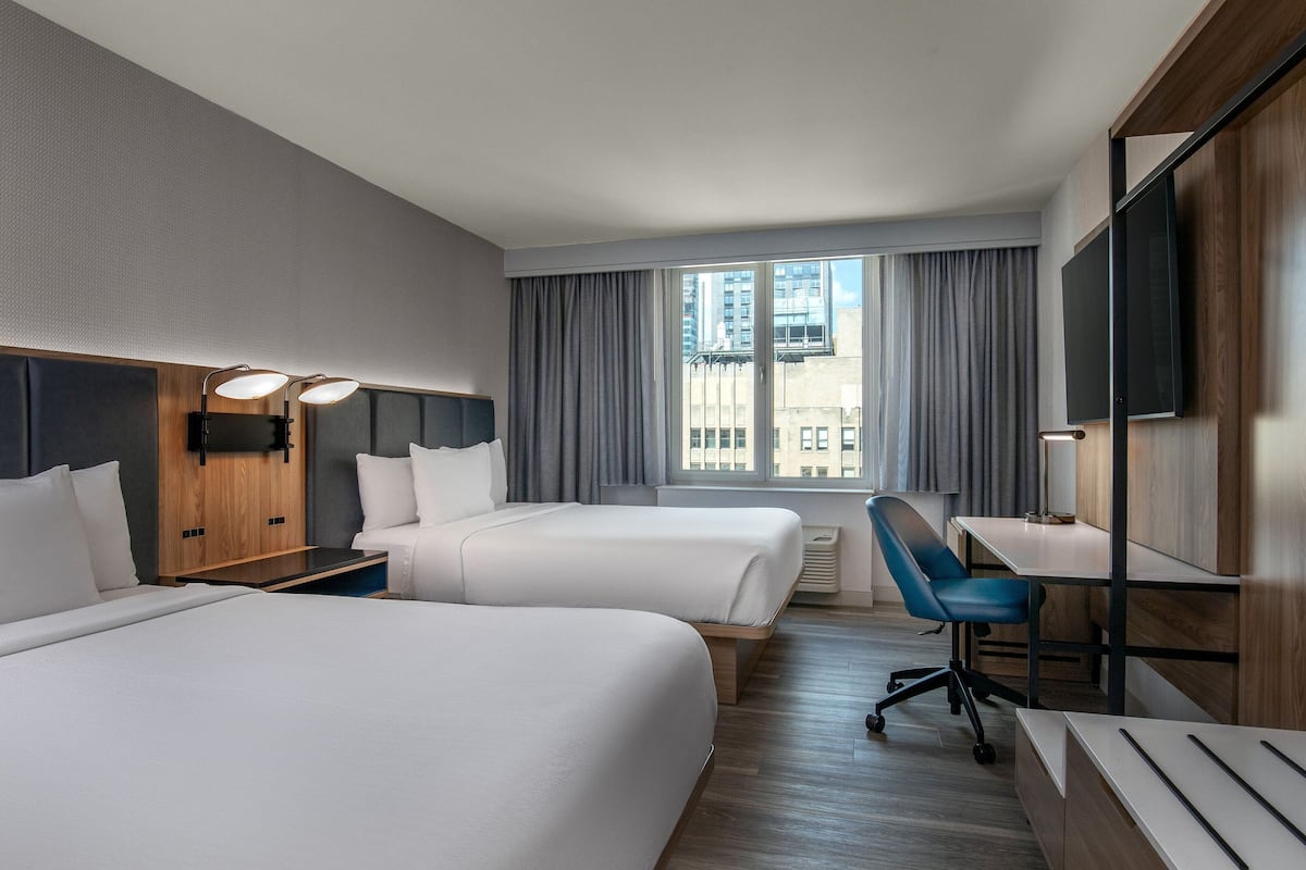 Een hotelkamer met twee bedden, een bureau, een stoel, een televisie en een raam met gordijnen.