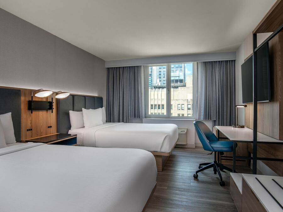 A hotel room with two beds, a desk, a chair, a TV, and a window with curtains.