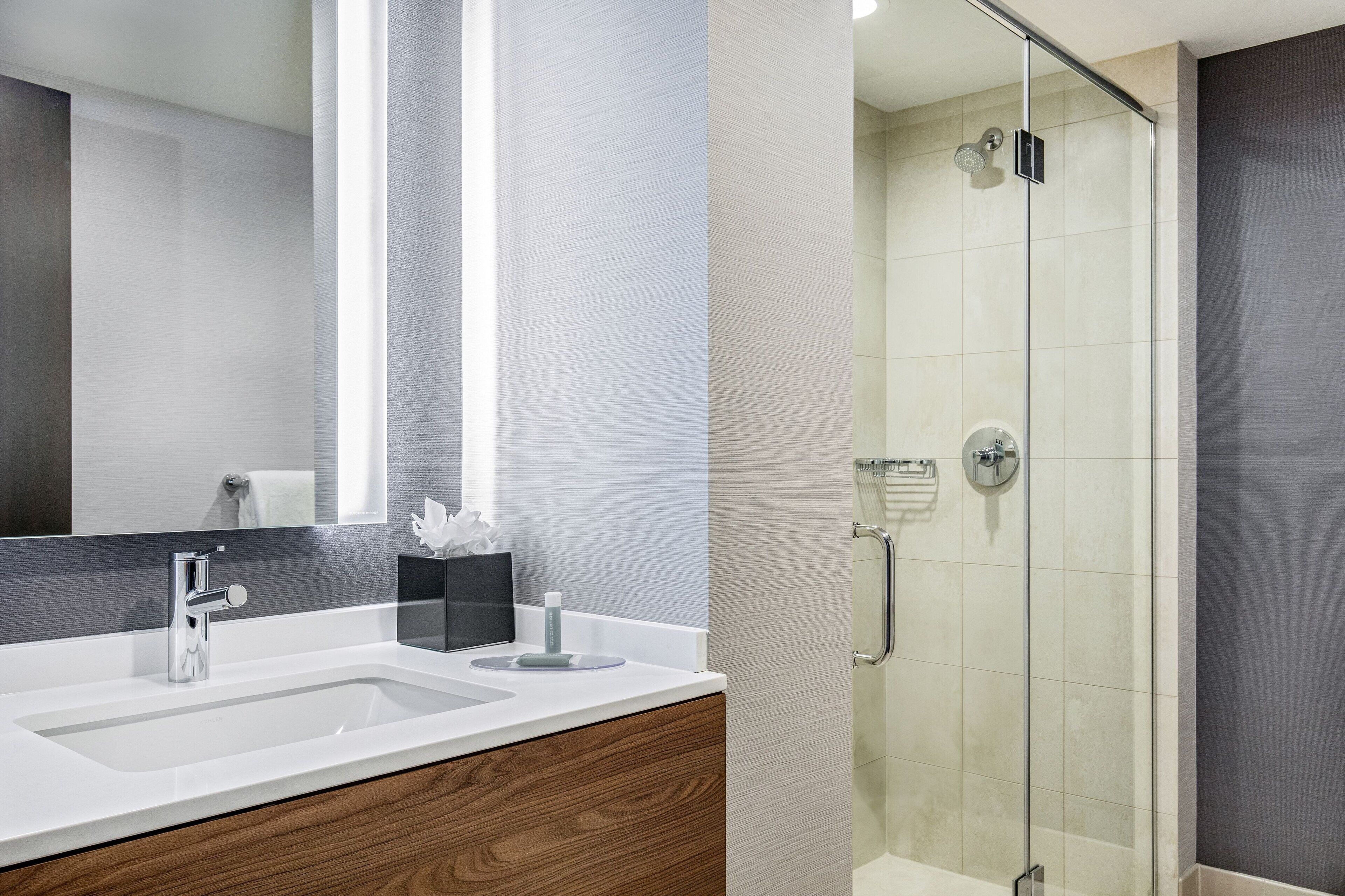 Un baño moderno con un espejo grande, dos lavabos y una ducha con mampara de vidrio.