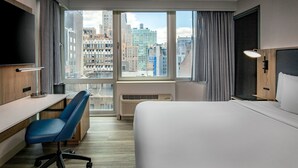 Een hotelkamer met een groot raam, een bed, een bureau, een stoel en een televisie.