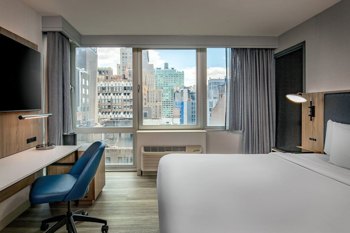 Een hotelkamer met een groot raam, een bed, een bureau, een stoel en een televisie.