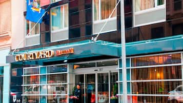 A Courtyard Marriott hotel with a glass facade, a flag, and a security guard outside.