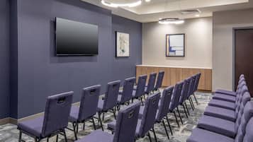A conference room with rows of purple chairs, a flat-screen TV, and framed artwork on the walls.