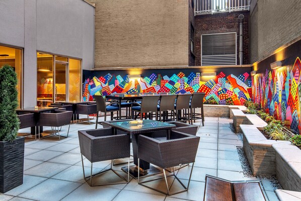 An outdoor patio area with tables and chairs, a colorful mural on the wall, and a brick building in the background. - Courtyard New York Manhattan/Times Square West (New York)