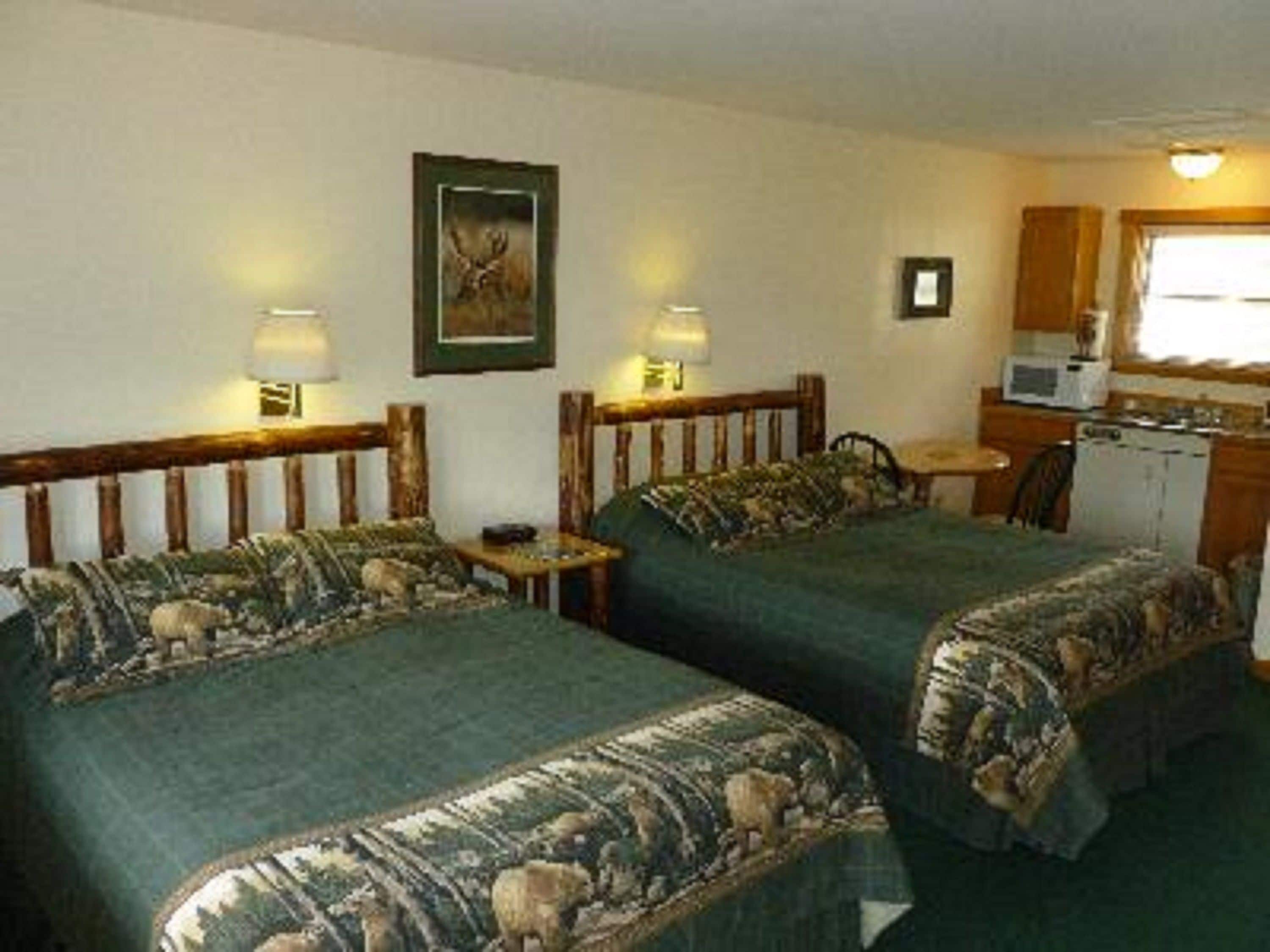 A room with two beds, a small kitchenette, and a framed picture on the wall.