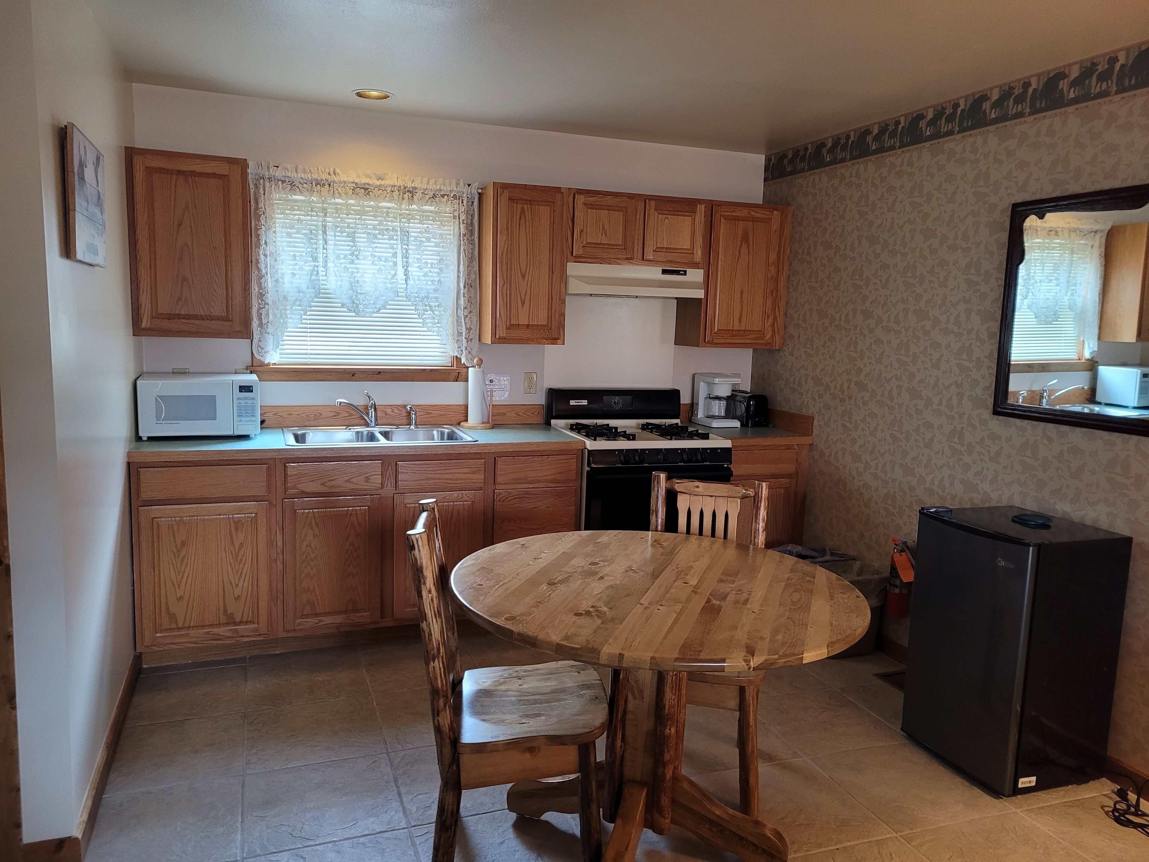 A compact kitchen with wooden cabinets, a stove, a microwave, and a dining table with chairs.