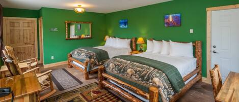 A room with two wooden beds, a wooden chair, a wooden table, a mirror, and a green wall.