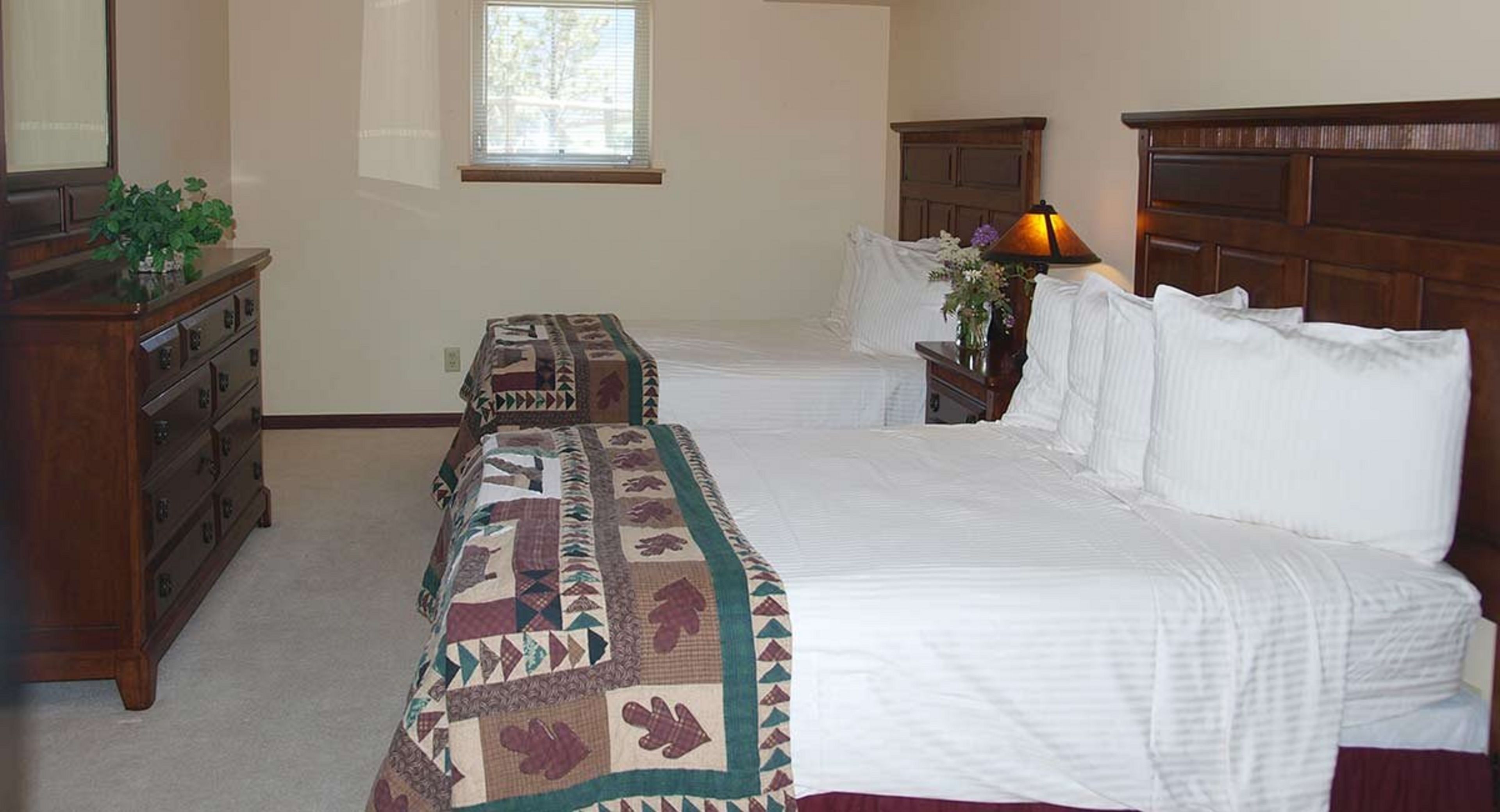 Quarto com duas camas, cômoda, mesa de cabeceira e uma janela.