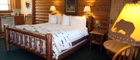 A log cabin-style room with a wooden bed, two bedside lamps, a small table, and a chair.