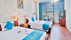 A hotel room with two beds, a desk, a chair, a window with a view, and a decorative wall. - Thanh Binh Trade Union Hotel (Da Nang)