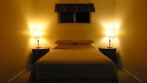 Habitación de hotel estrecha con una cama centrada entre dos mesitas de noche, cada una con una lámpara.