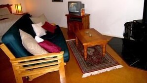 Una sala de estar con un sofá azul, una mesa de centro de madera y un televisor sobre un mueble de madera.
