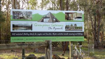 A signboard for Grampians Getaway The Pyramids, featuring a mountain, a house, and a playground. It mentions self-contained holiday units, onsite activities like canoeing and fishing, and provides contact information.