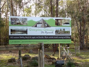 A signboard for Grampians Getaway The Pyramids, featuring a mountain, a house, and a playground. It mentions self-contained holiday units, onsite activities like canoeing and fishing, and provides contact information. - Grampians Getaway Resort (Halls Gap)