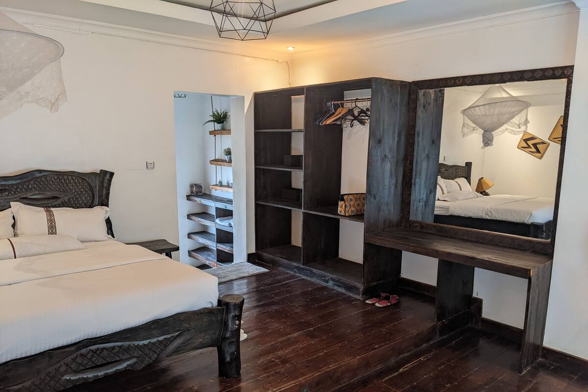 A bedroom with a bed, a wooden bench, a shelf with plants, and a wardrobe.