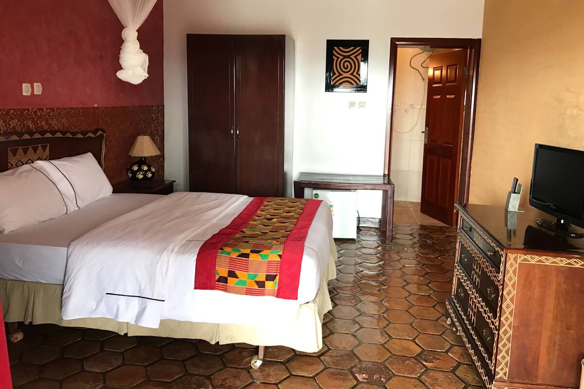 A hotel room with a large bed, a wardrobe, a desk with a computer, and a television.