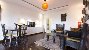 A modern living room with a dark wood floor, a round orange pendant light, and a variety of seating options including a sofa and chairs. - Inside Afrika Boutique Hotel (Kigali)