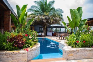 A swimming pool surrounded by stone planters with tropical plants and a palm tree. - Inside Afrika Boutique Hotel (Kigali)