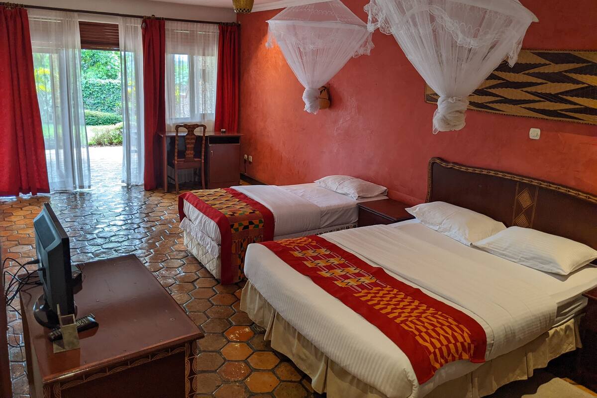 A hotel room with two beds, a desk with a computer, and a view of a garden through a glass door.