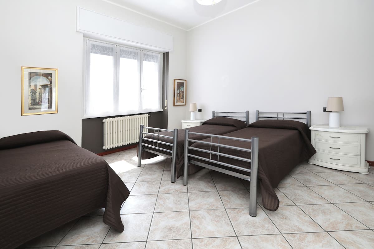 A bedroom with a bed, a bedside table, a lamp, a radiator, and a window.