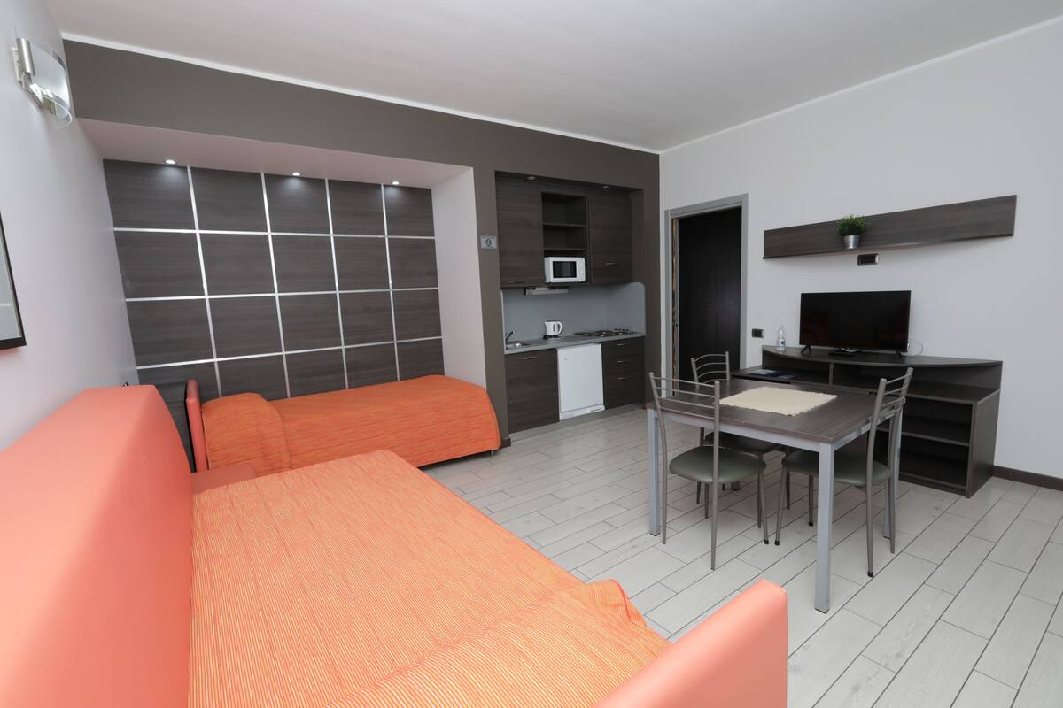 A modern hotel room with a bed, a desk, a chair, a TV, and a microwave.