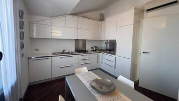Una cocina moderna con armarios blancos, electrodomésticos de acero inoxidable y un comedor con mesa y sillas.