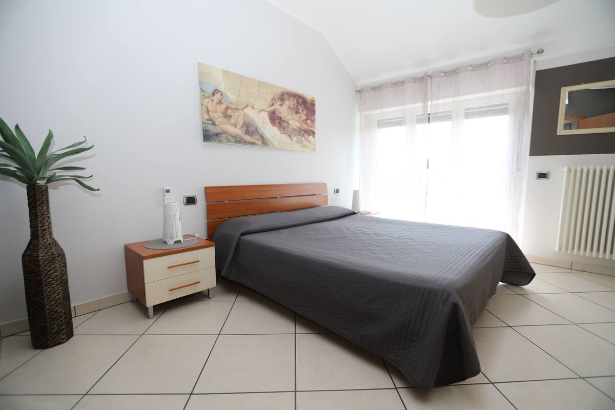 A bedroom with a bed, a nightstand, a plant, a painting, and a radiator.