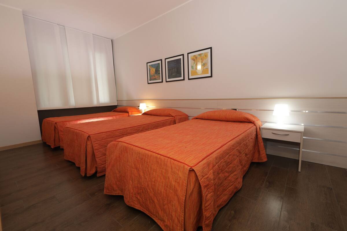 A hotel room with two beds, a nightstand, and a window with curtains.
